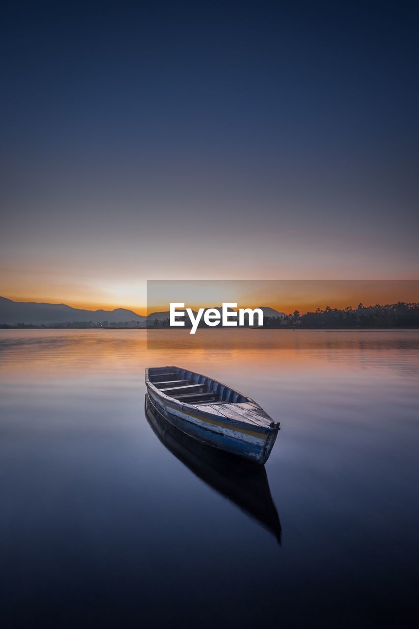 Boat moored in lake against sky during sunset