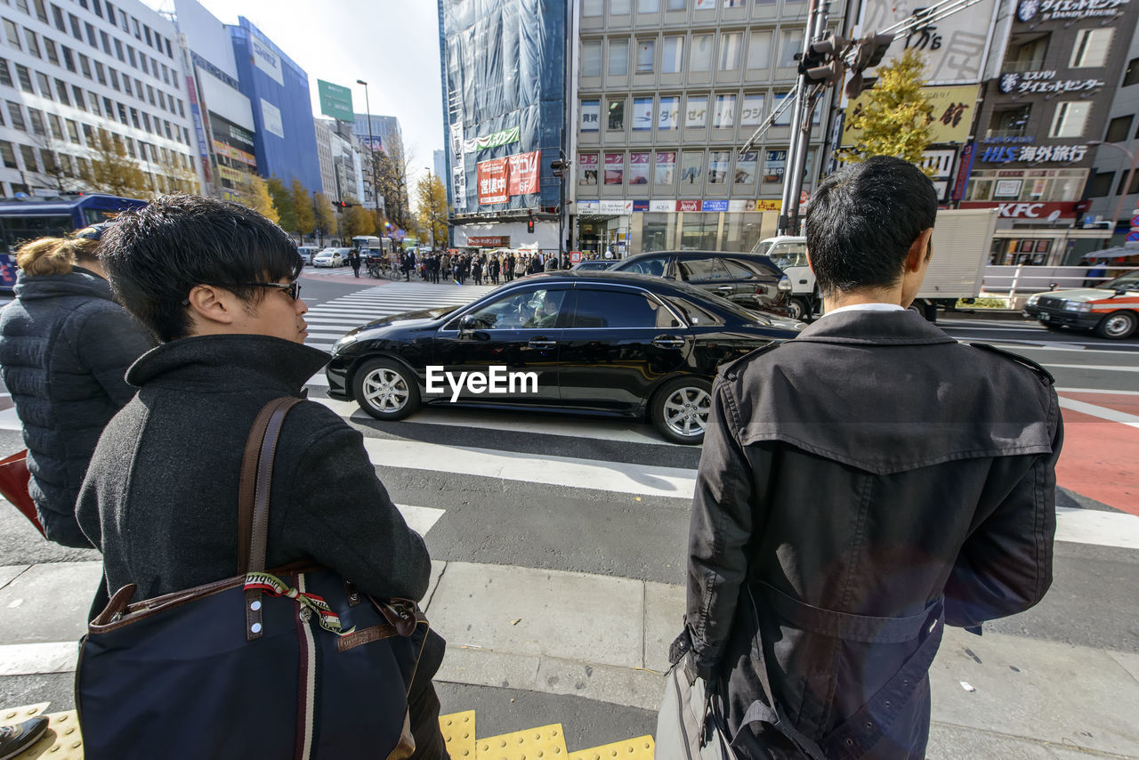 REAR VIEW OF PEOPLE STANDING ON STREET IN CITY