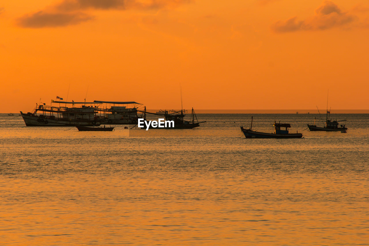 Silhouette boat sailing on sea against orange sky