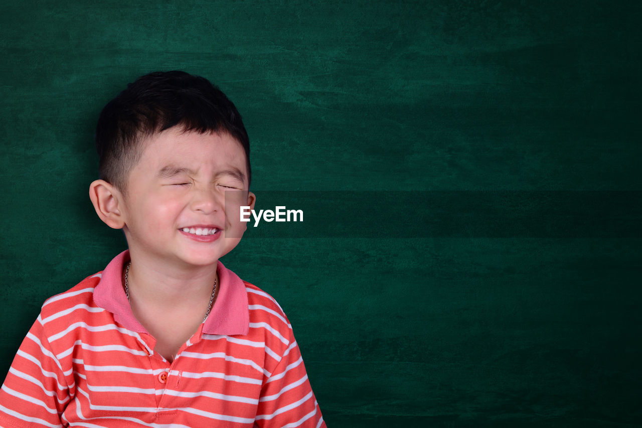 Cute boy with eyes closed against blackboard