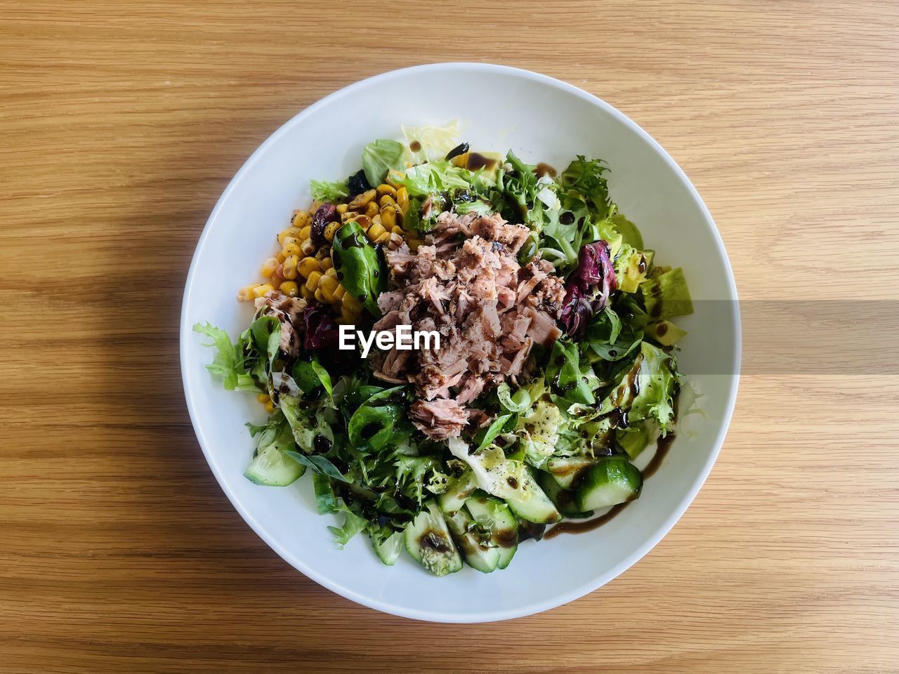High angle view of a salad with greens and tuna in plate on wooden table
