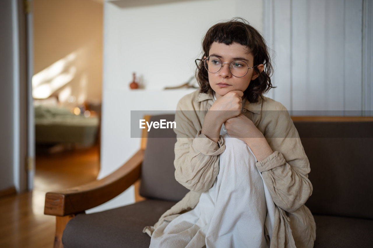 portrait of young woman looking away while sitting on sofa at home