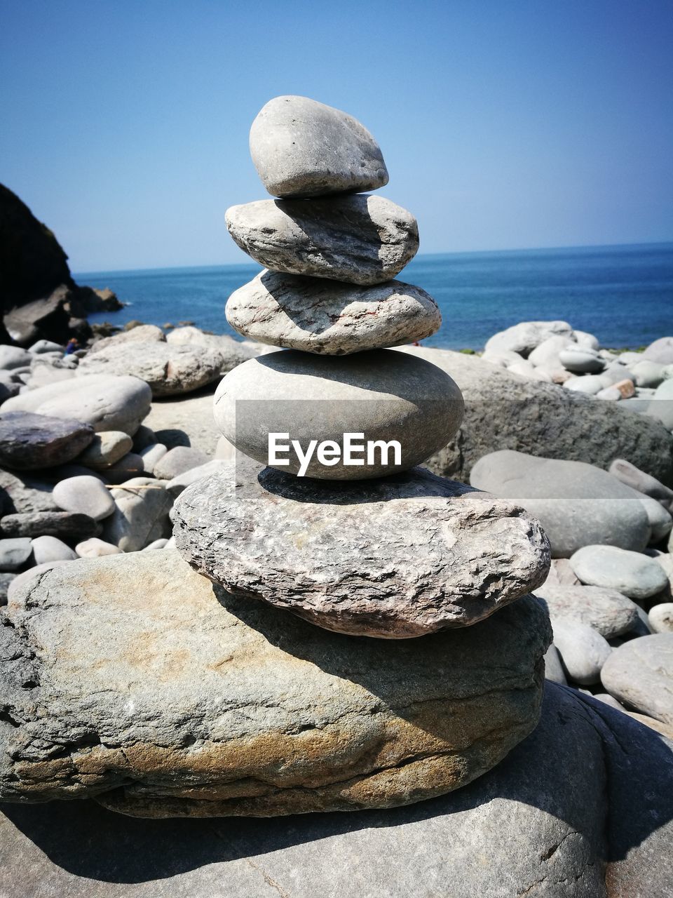 Stack of pebbles at beach against clear blue sky during sunny day