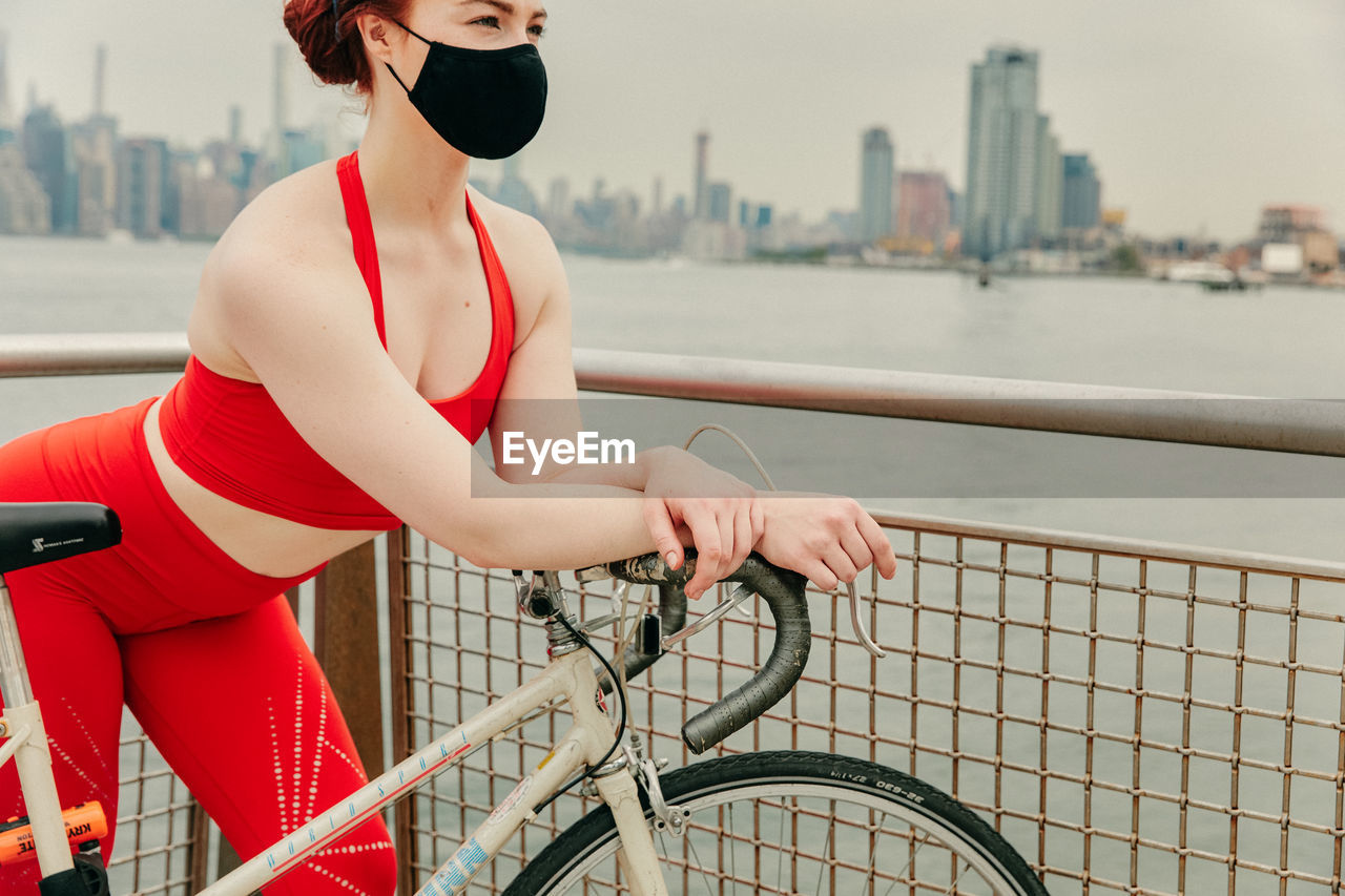Young female cyclist wearing face mask with bike by waterfront