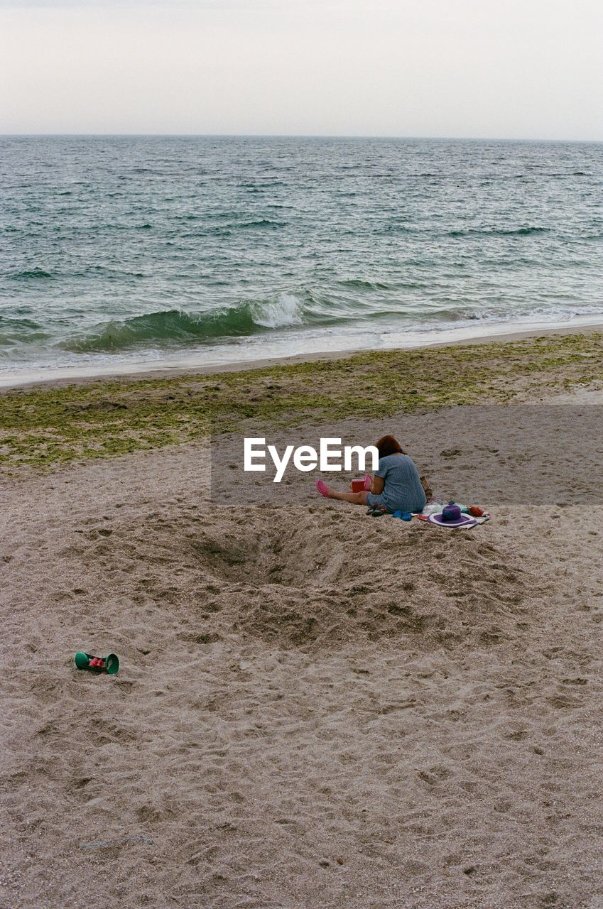 REAR VIEW OF CHILDREN SITTING ON BEACH