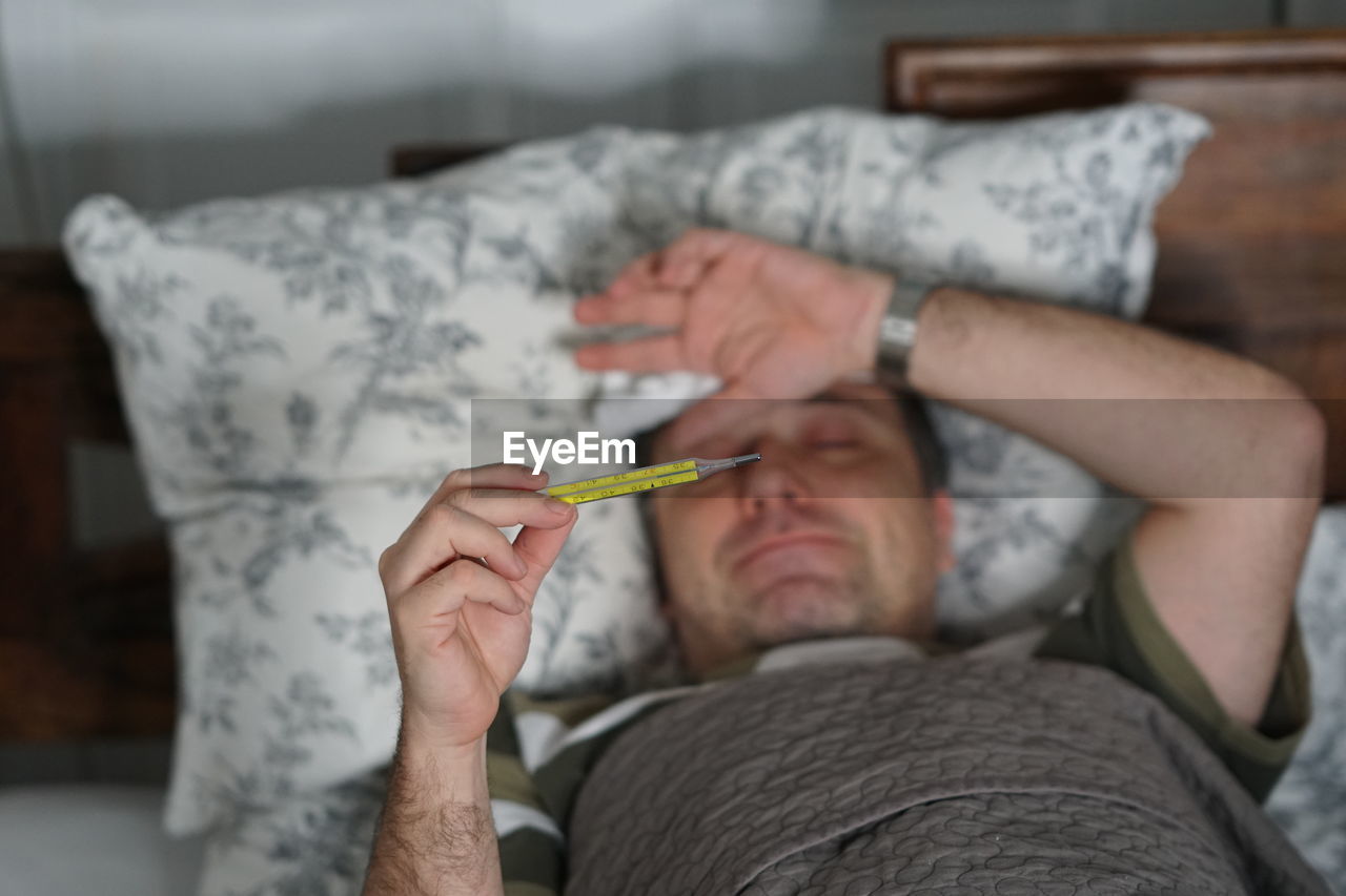 Man checking temperature while lying on bed at home