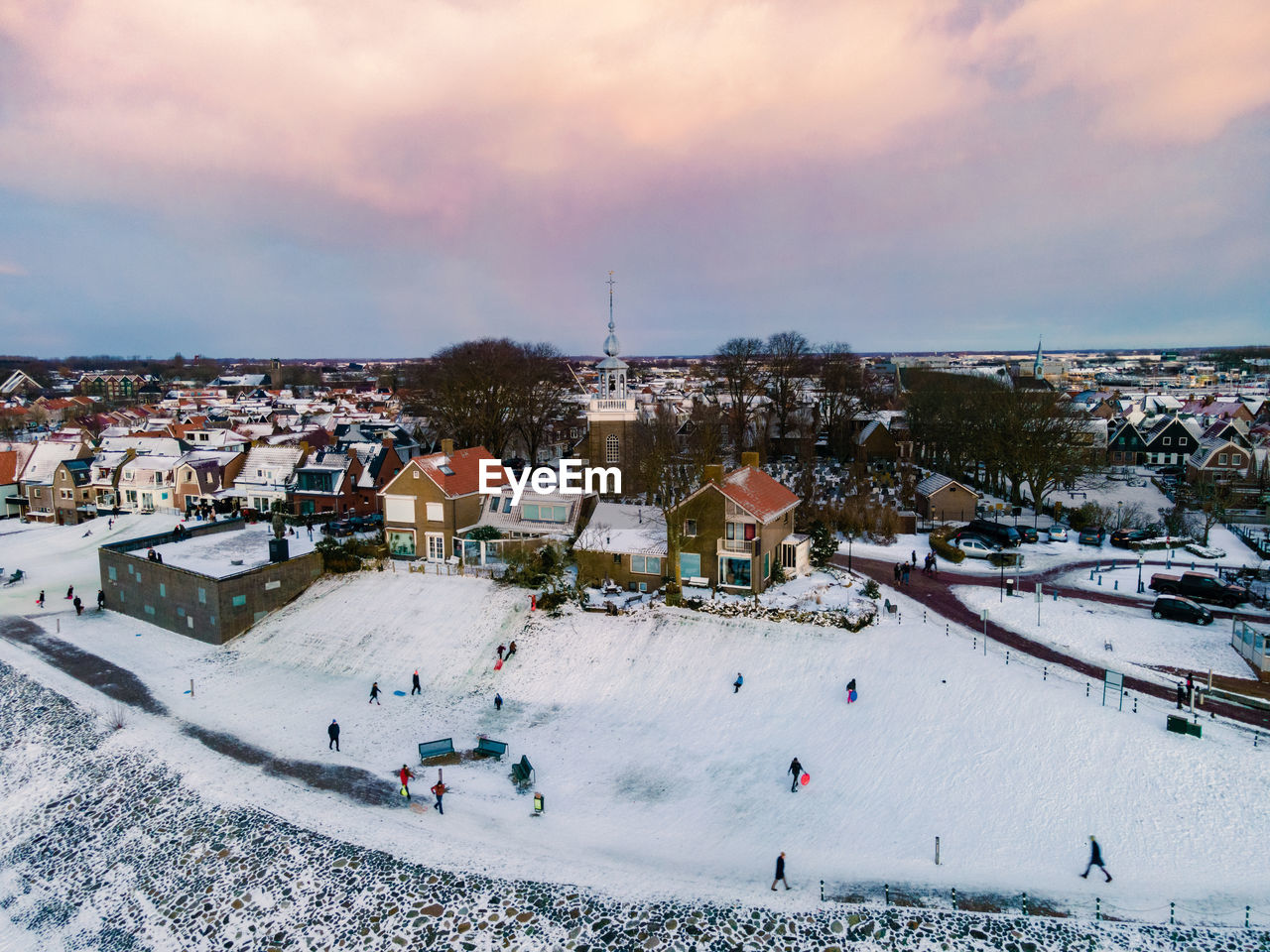 HIGH ANGLE VIEW OF PEOPLE ON SNOW IN CITY AGAINST SKY