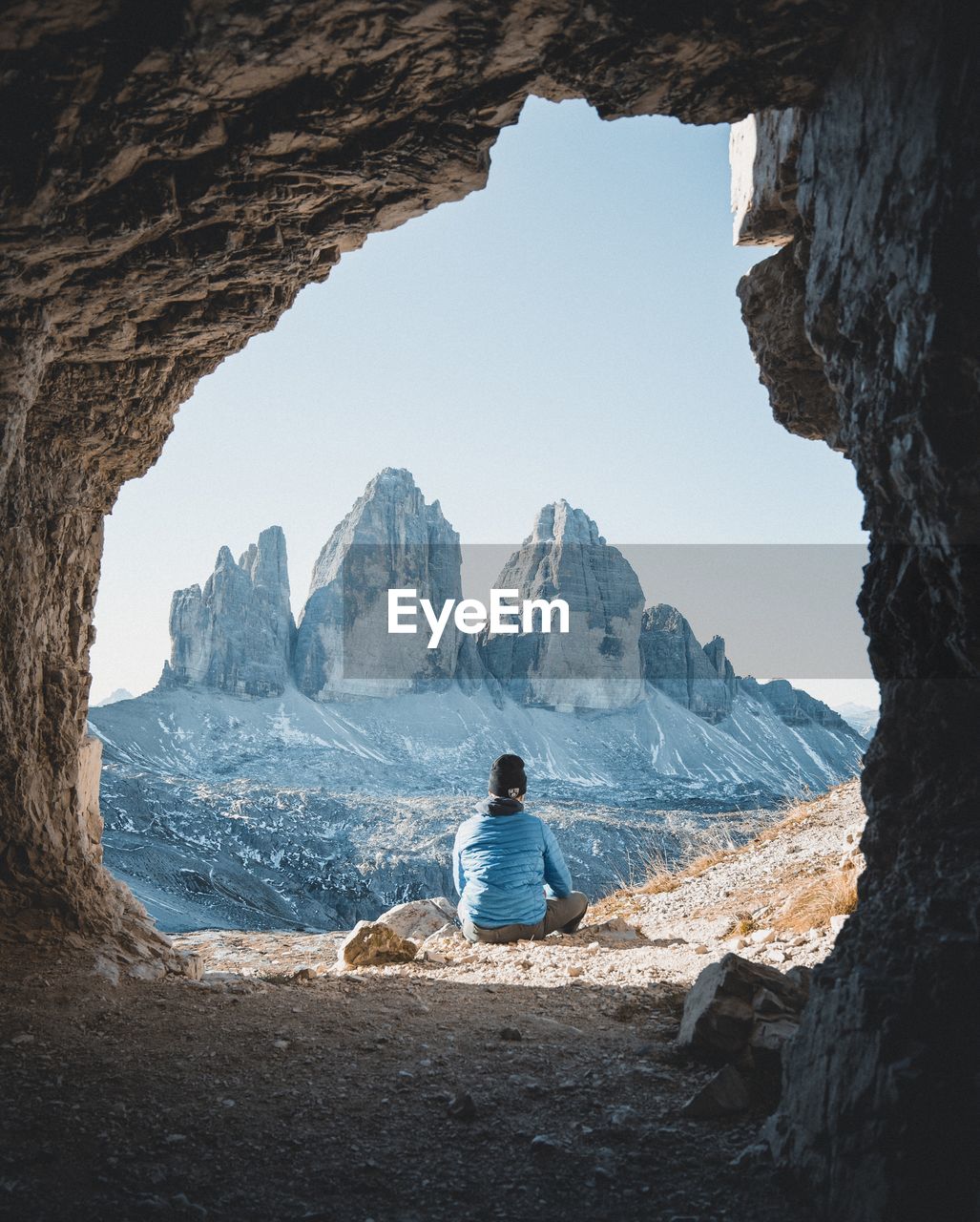 Rear view of man sitting on rock while looking at mountains