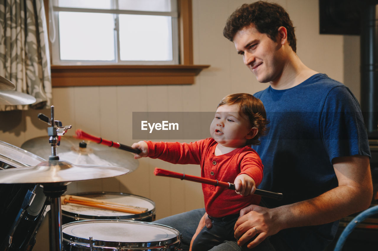 Son playing drums while sitting with father at home