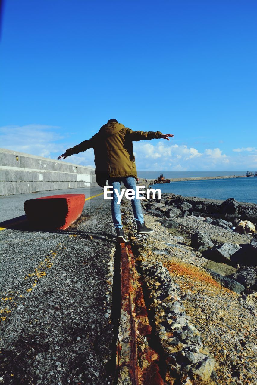 Rear view of man walking by sea against blue sky