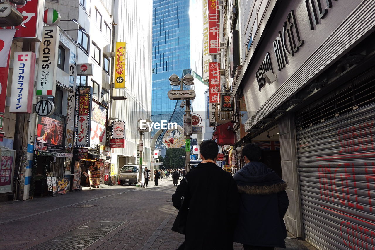 REAR VIEW OF PEOPLE WALKING ON STREET AGAINST BUILDINGS