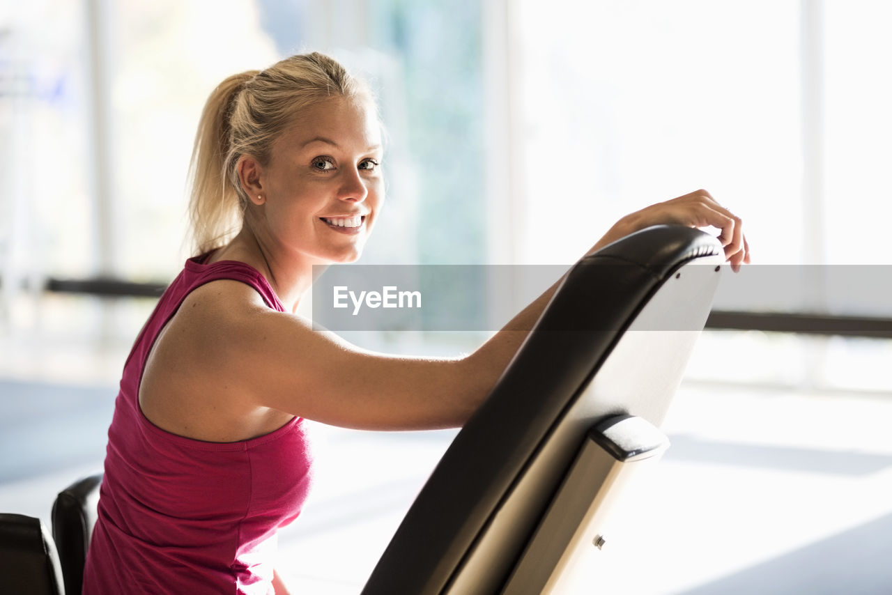 Portrait of smiling young woman sitting on chair at gym