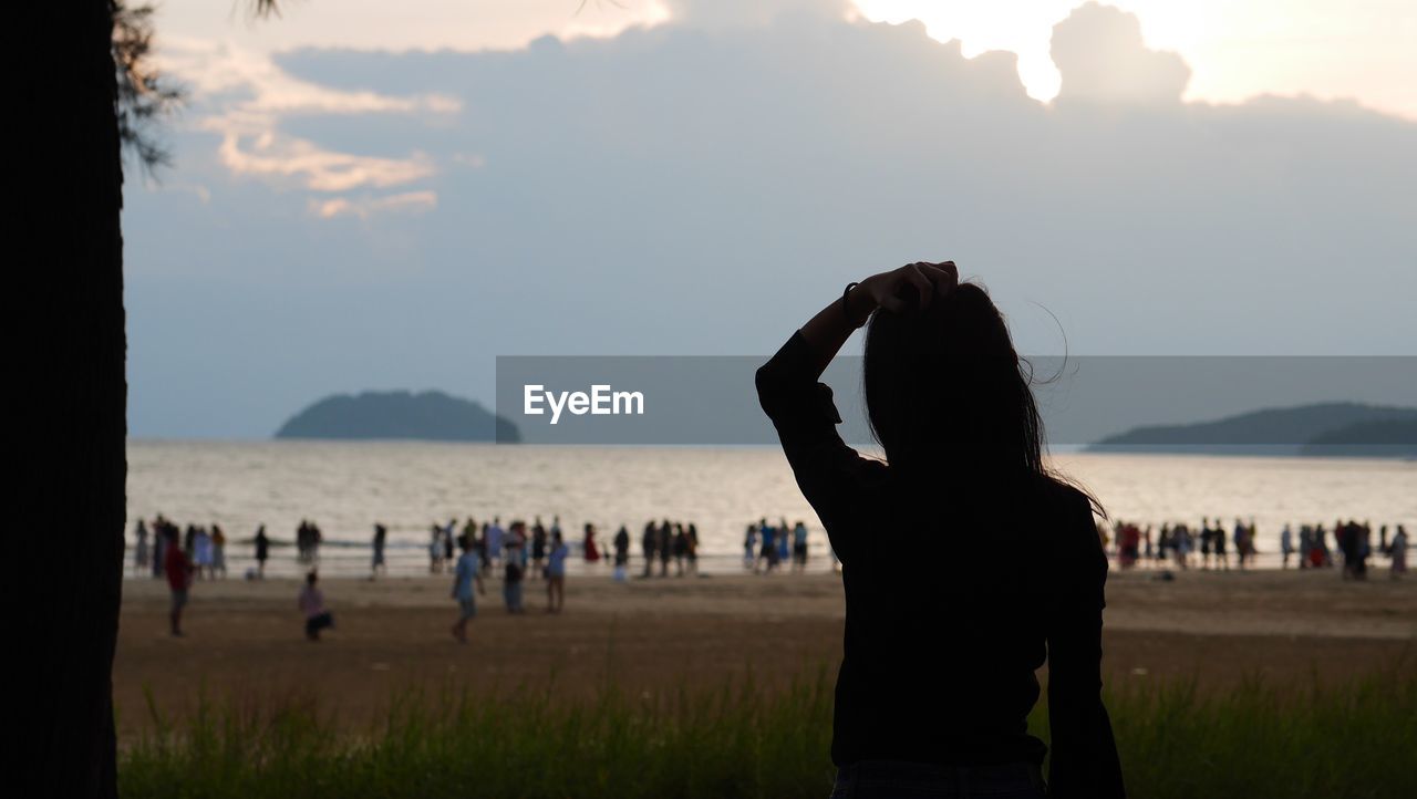 Silhouette woman looking people at beach against sky