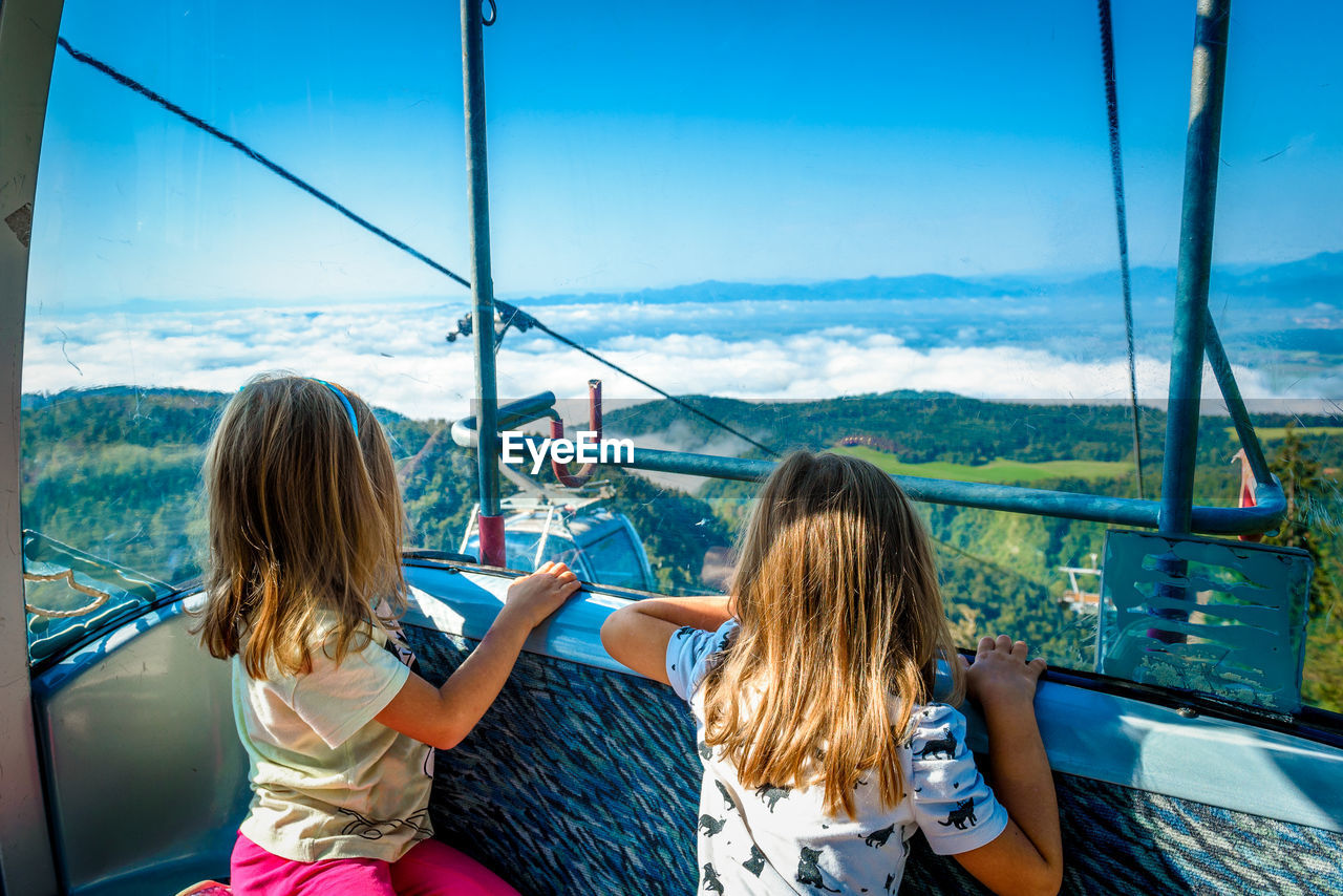 Girls traveling in overhead cable car against sky