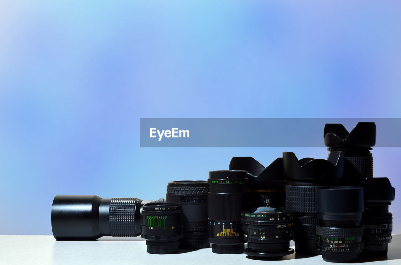 Close-up of camera and lenses on table against blue background