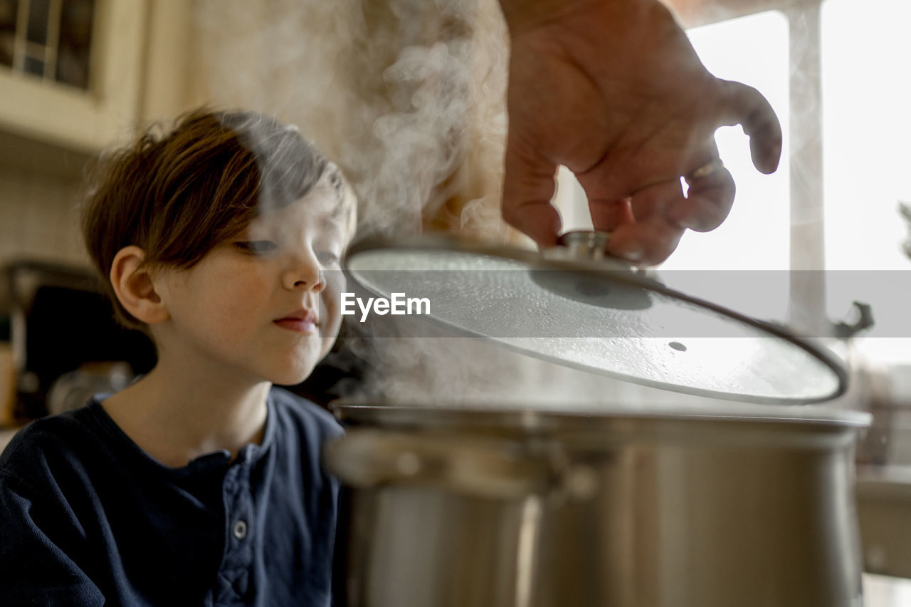 Son smelling hot soup in kitchen at home