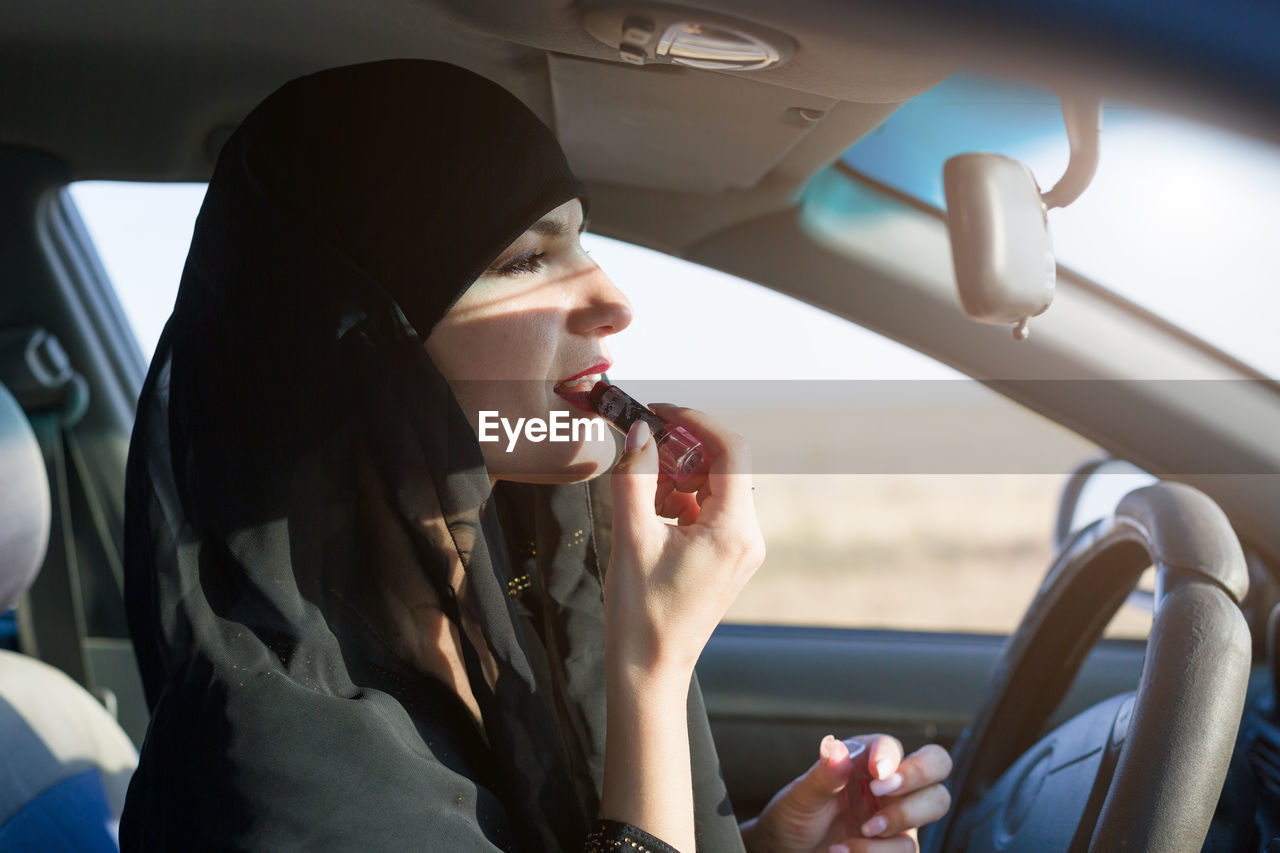 Smiling woman applying lipstick while sitting at car