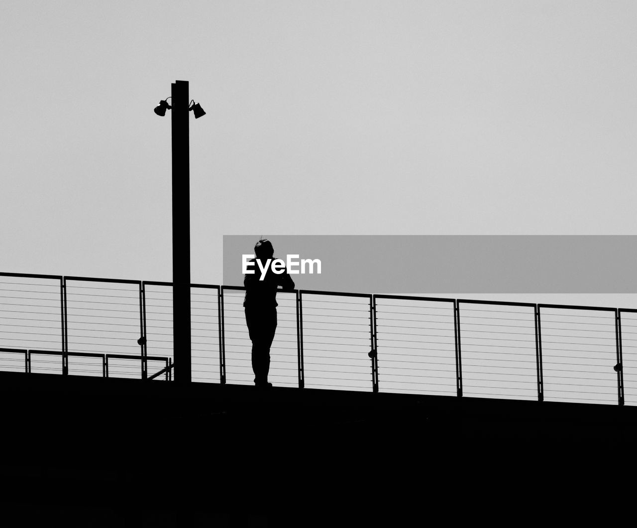 Silhouette man standing on bridge against clear sky
