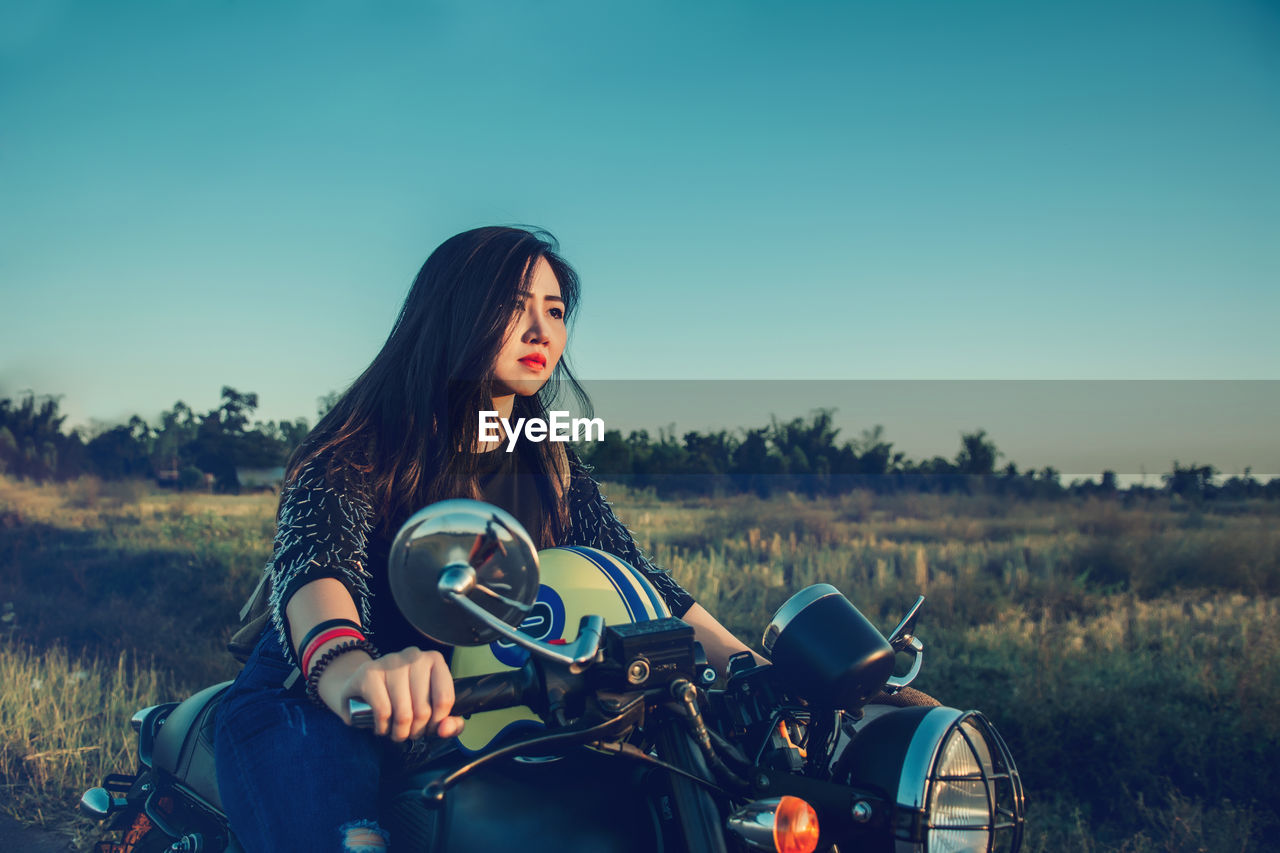 Woman riding motorcycle on field against clear sky