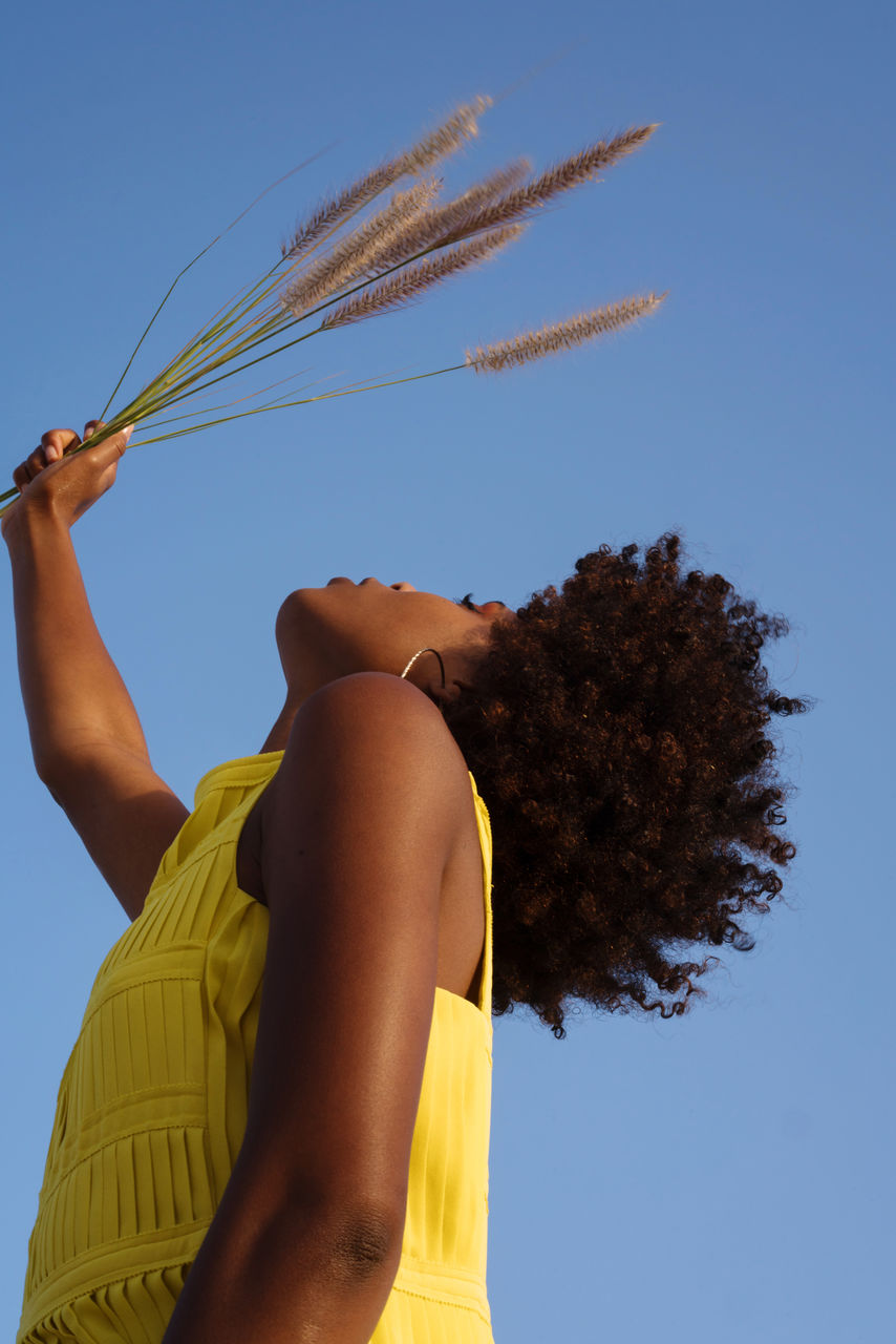 Portrait of a young black woman wearing yellow dress holding grass