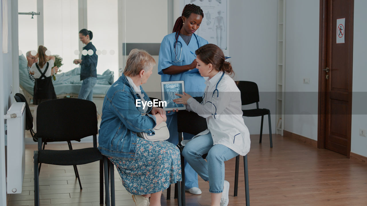 side view of female friends using digital tablet while sitting on chair