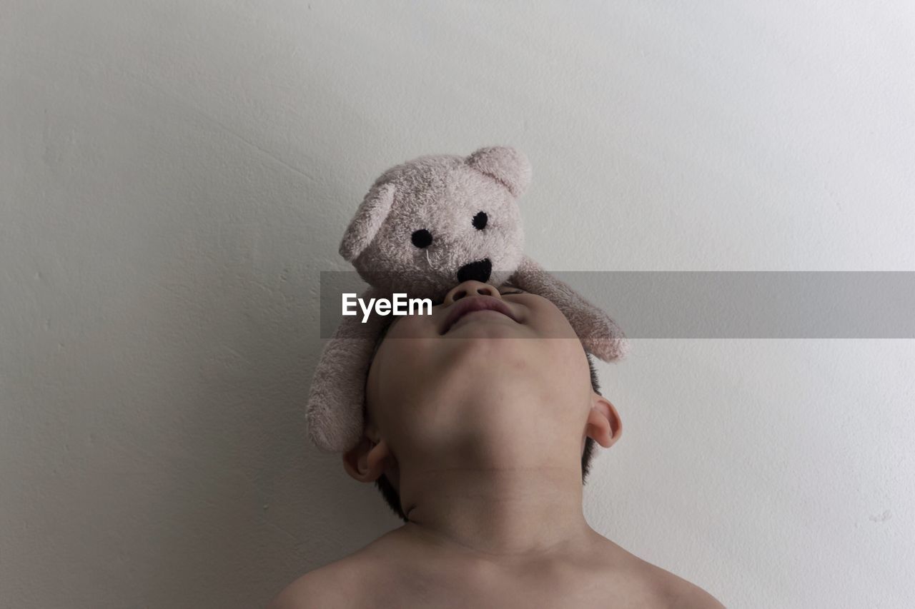 Teddy bear on boy face against wall at home