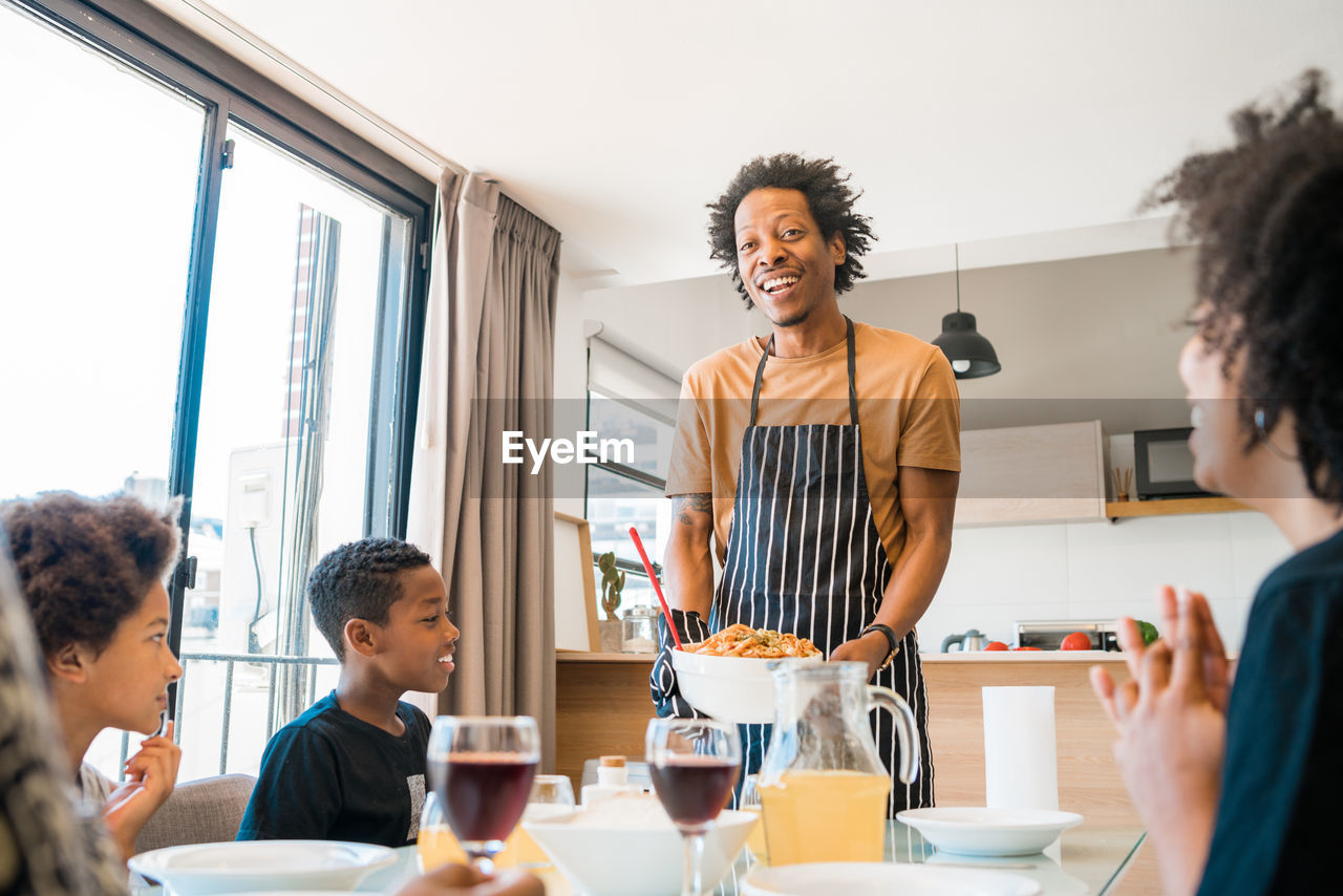 Cheerful man serving food to family at dining table