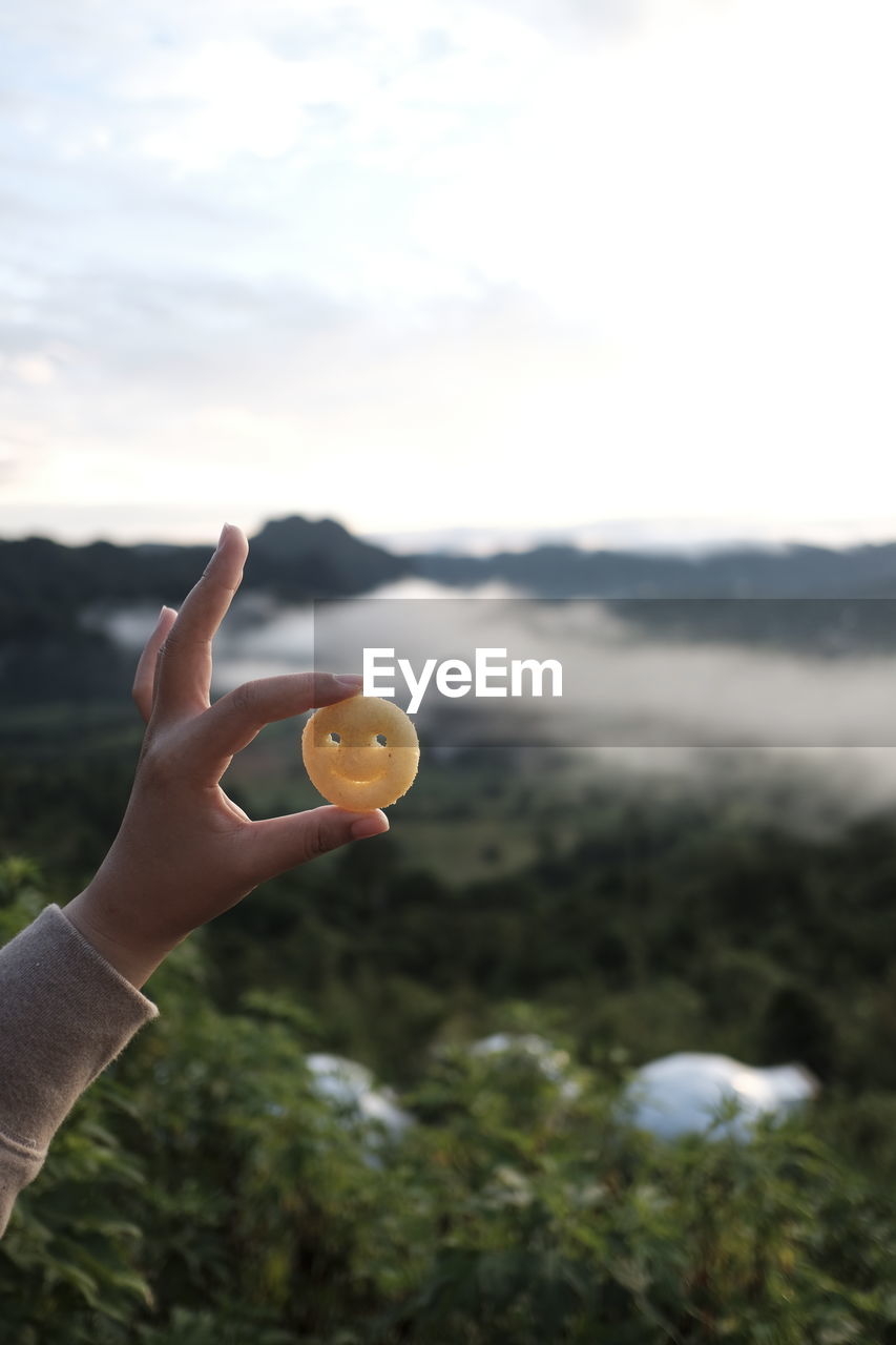HAND HOLDING BALL AGAINST SKY