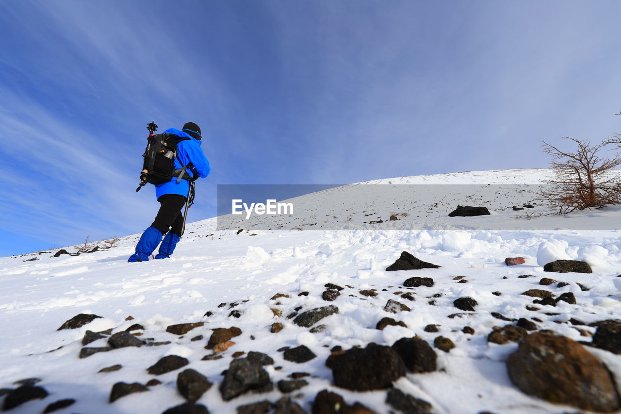 snow, winter, cold temperature, mountain, sports, leisure activity, one person, nature, adventure, sky, activity, full length, adult, environment, winter sports, vacation, holiday, landscape, clothing, mountaineering, motion, scenics - nature, mountain range, trip, extreme sports, men, beauty in nature, travel, lifestyles, blue, day, hiking, backpack, skiing, snowcapped mountain, travel destinations, footwear, vitality, recreation, warm clothing, outdoors, sports clothing, ski mountaineering, person, copy space, young adult, climbing, rock, non-urban scene, sunlight, land, challenge, sports equipment, extreme terrain, exploration, ski touring