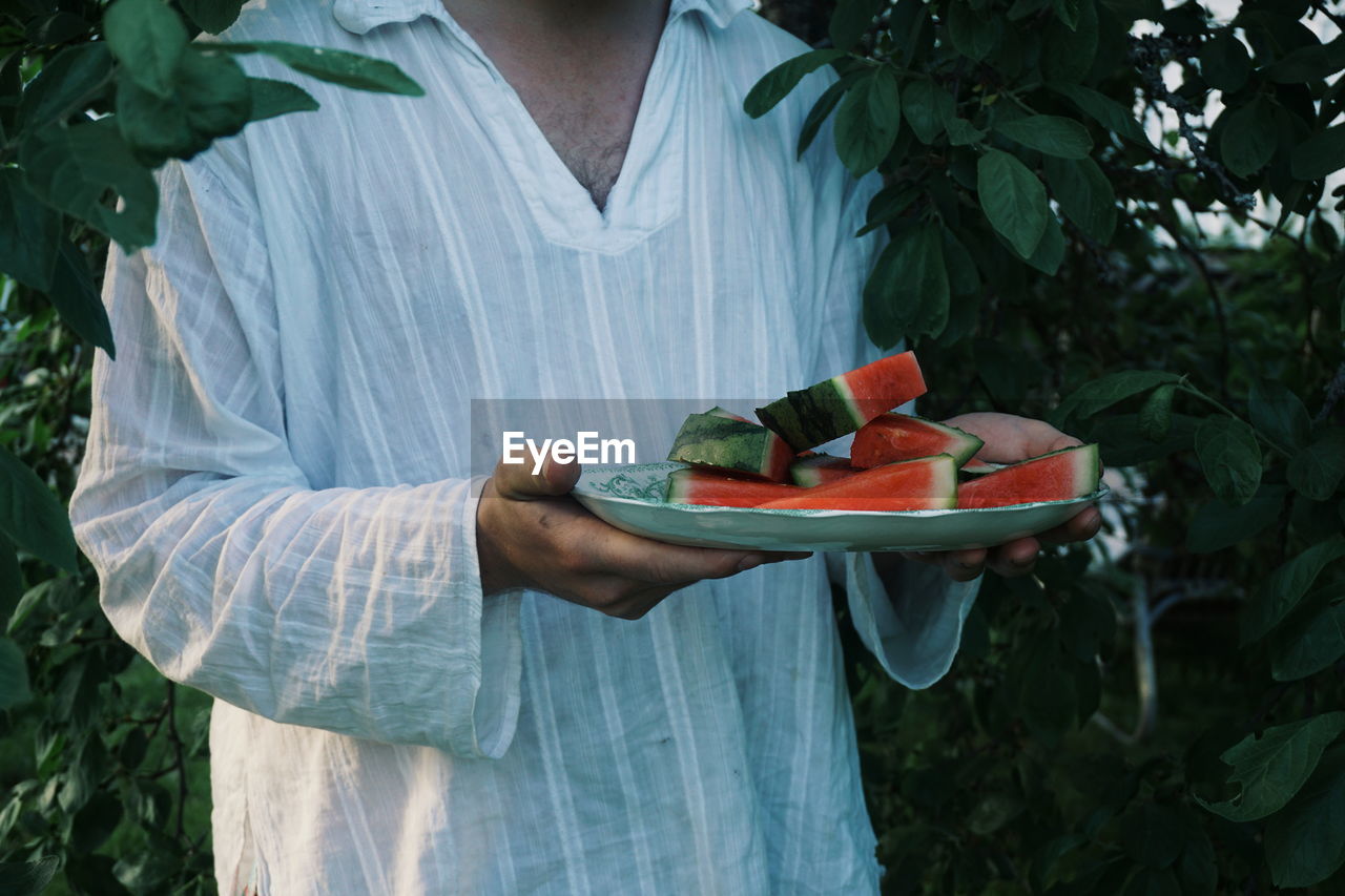 Midsection of person holding watermelon slices against plants