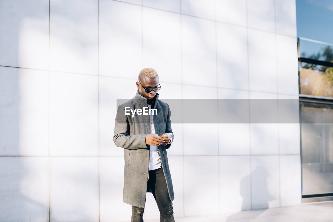 Handsome african boy with raincoat, sunglasses and mobile phone.