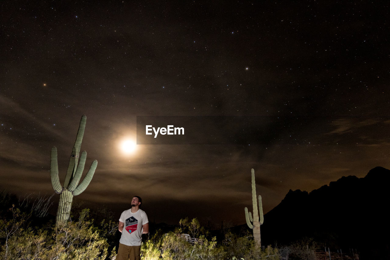 REAR VIEW OF MAN STANDING AGAINST SKY AT NIGHT