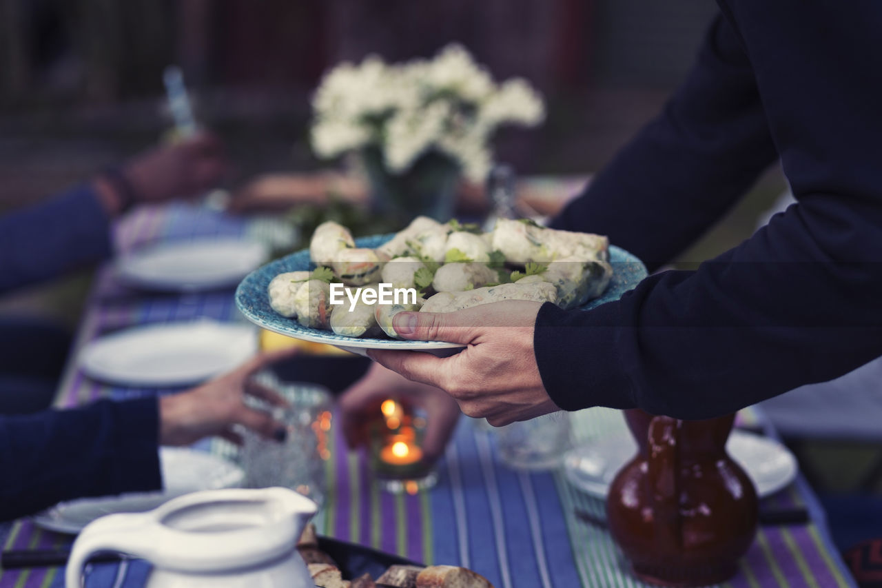 Cropped image of man holding plate with rice paper rolls at outdoor food table during party