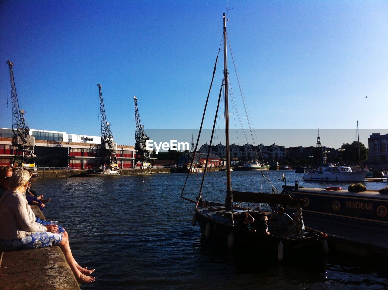 People sitting on pier at harbor against sky