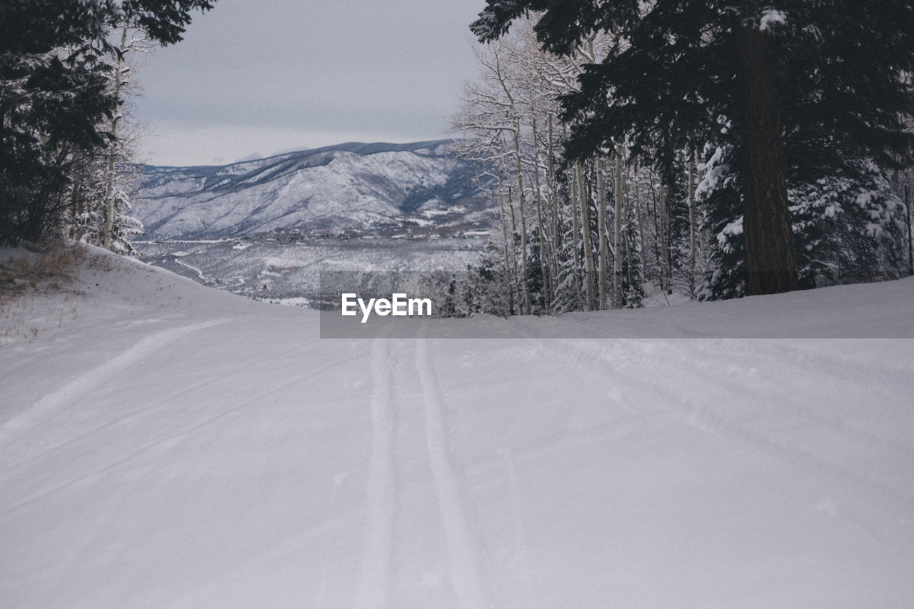 Road by snow covered landscape against sky