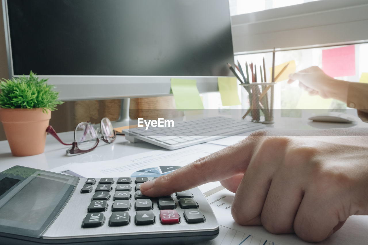 Cropped hand of businesswoman using calculator on table