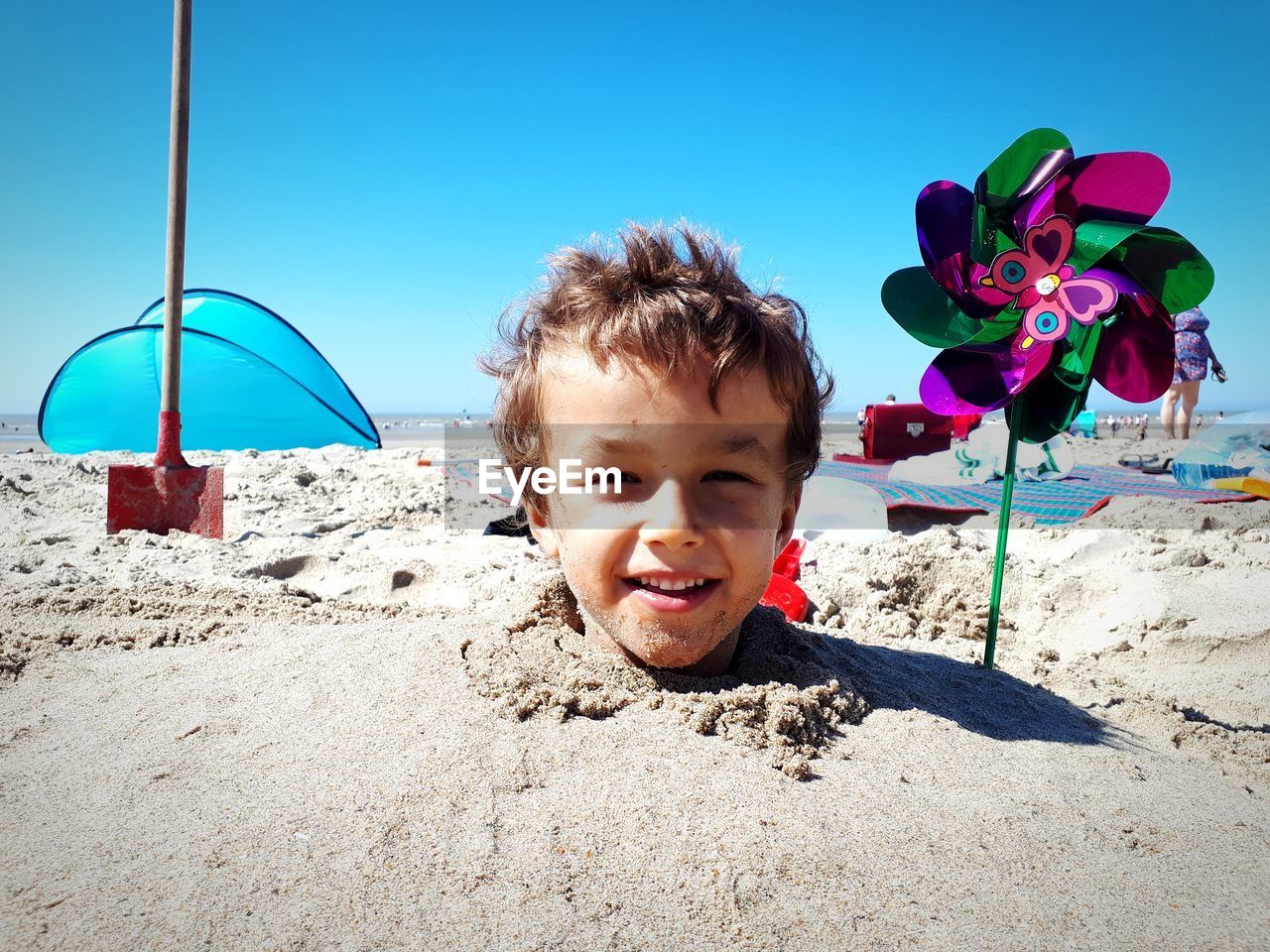 Portrait of cute boy buried in sand at beach against sky during sunny day