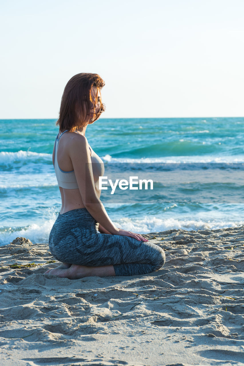 Young woman kneeling on shore at beach