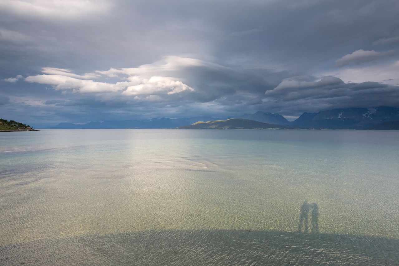 Shadow of people on river against cloudy sky