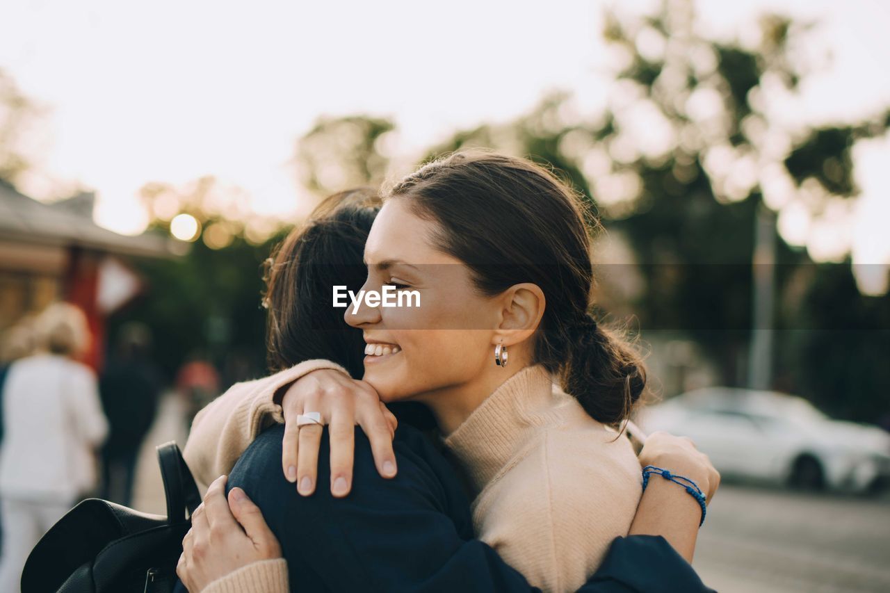 Smiling young woman embracing female friend in city