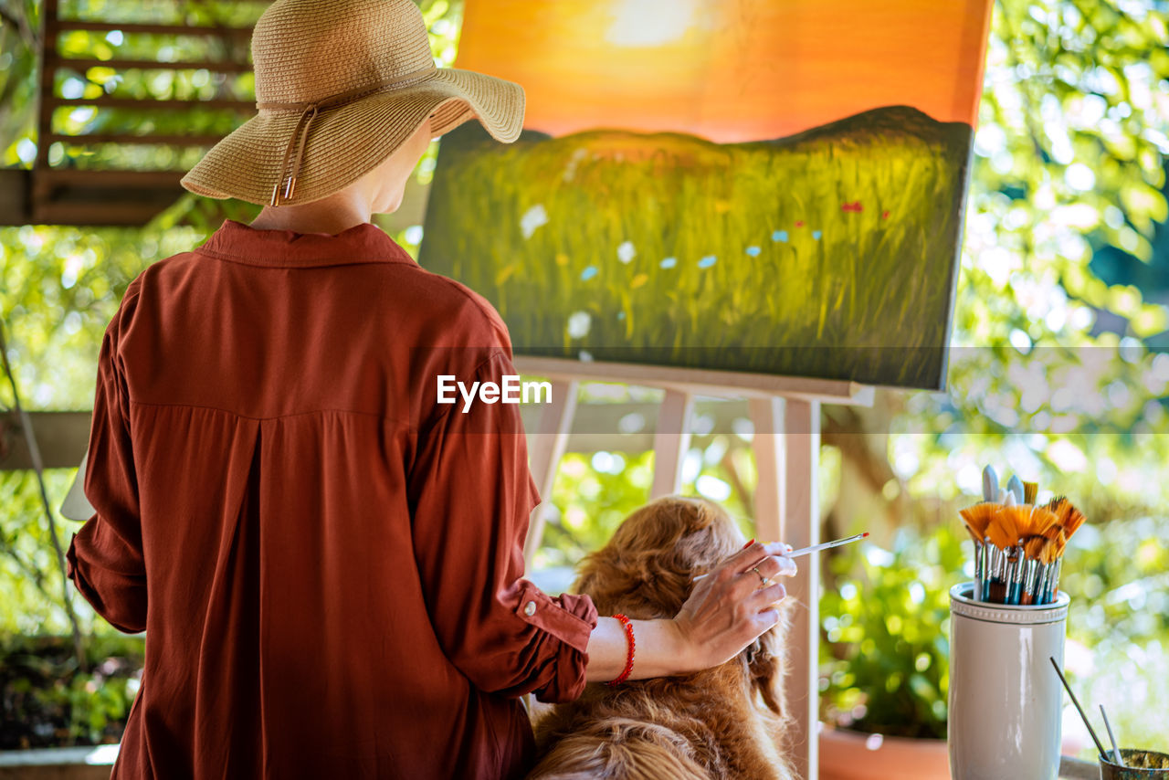 Young female artist working on her art canvas painting outdoors in her garden. creativity concept.