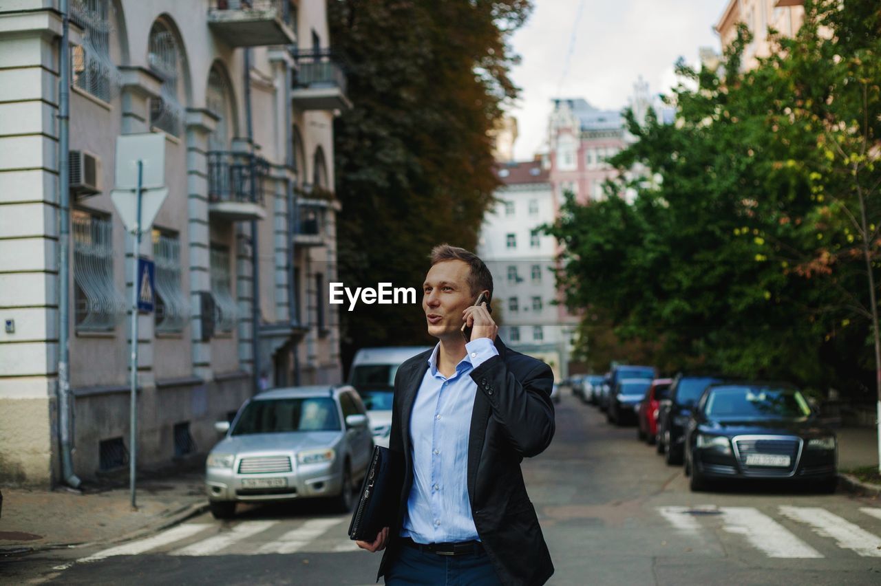 Businessman talking over smart phone while standing on road in city