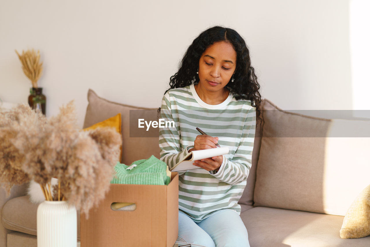 African-american female keeping count for clothing in cardboard box. moving away and packing