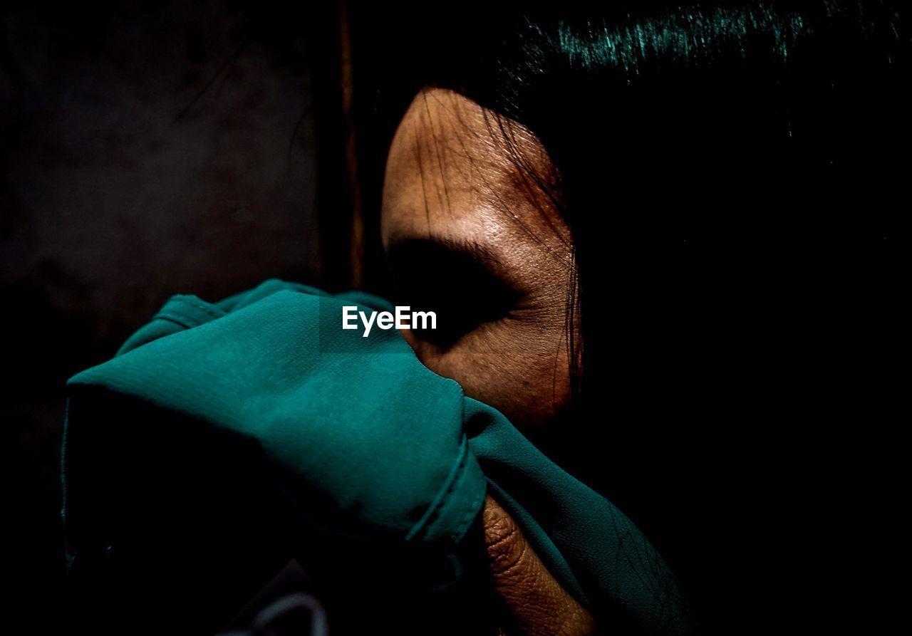 Close-up of woman covering mouth with green fabric in darkroom