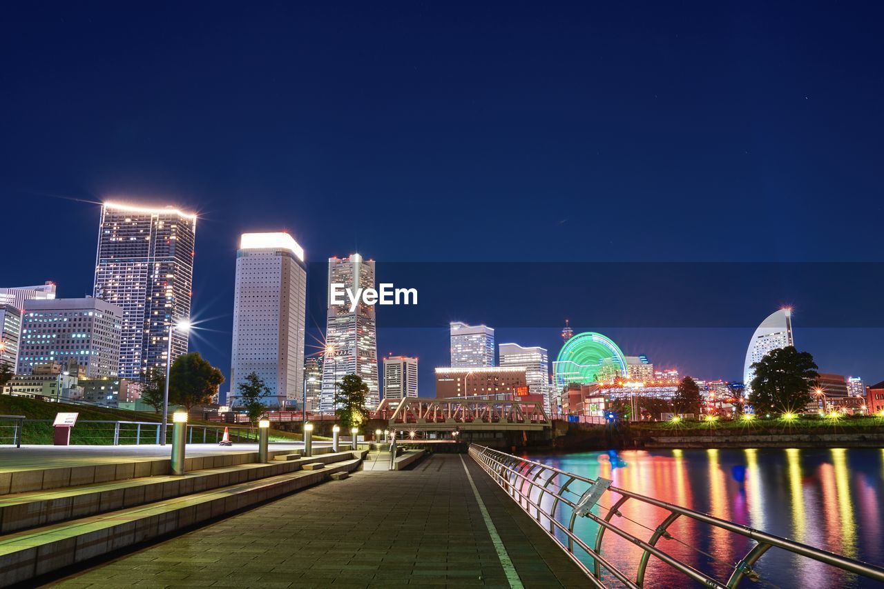 Illuminated bridge over river by buildings against sky at night
