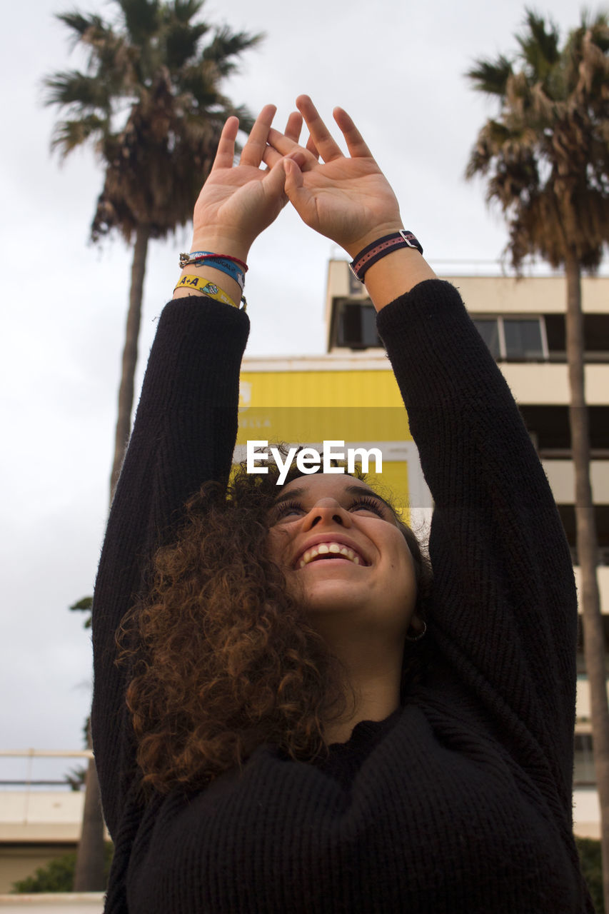 Smiling young woman with arms raised in city