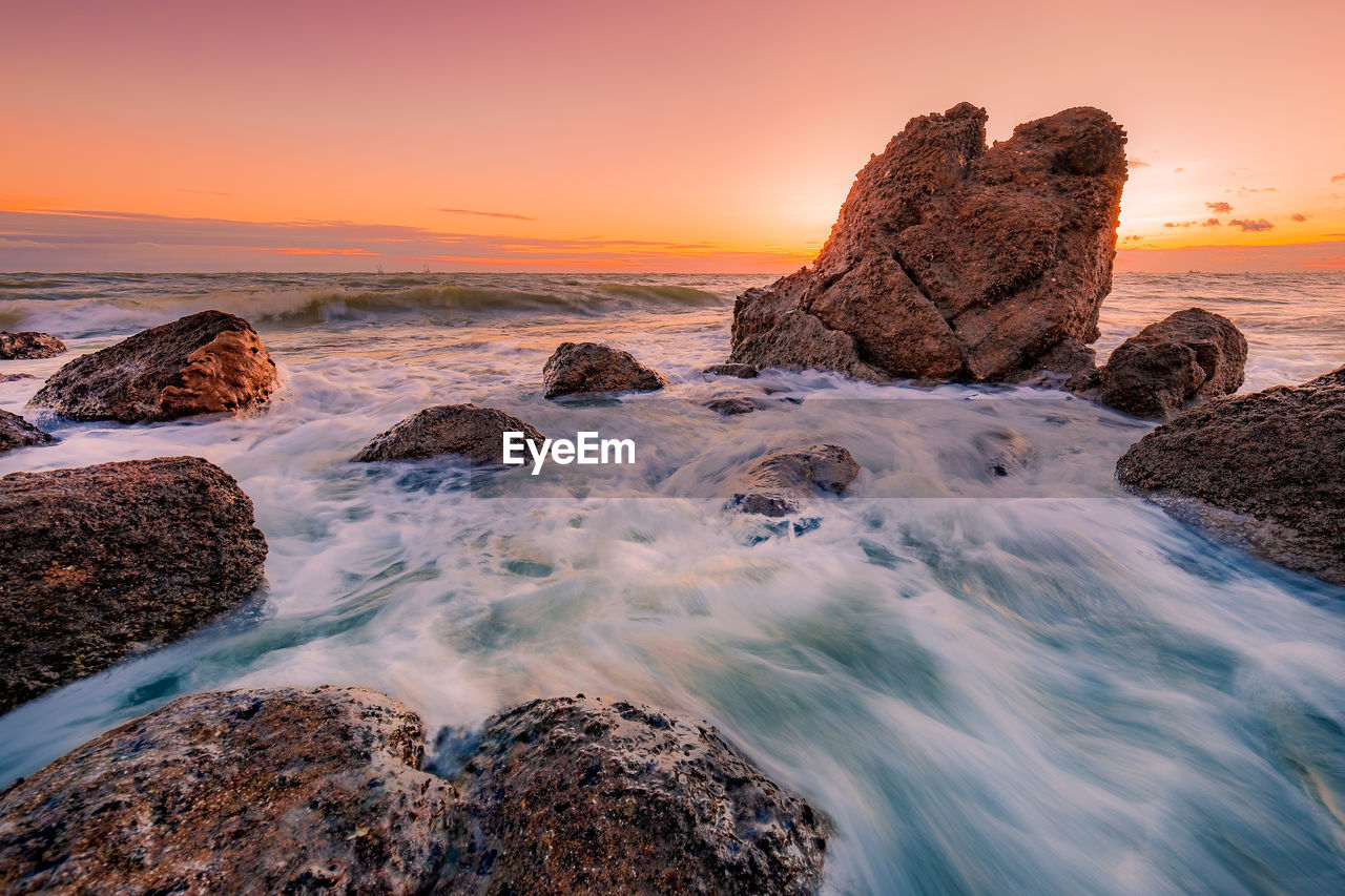 Rocks on beach against sky during sunset