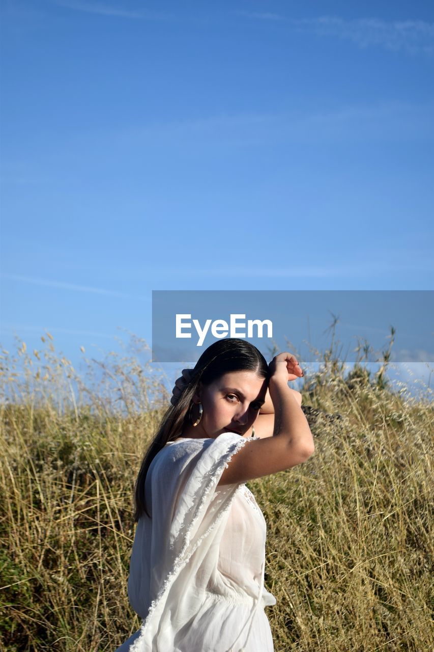 Young woman standing on field against clear blue sky