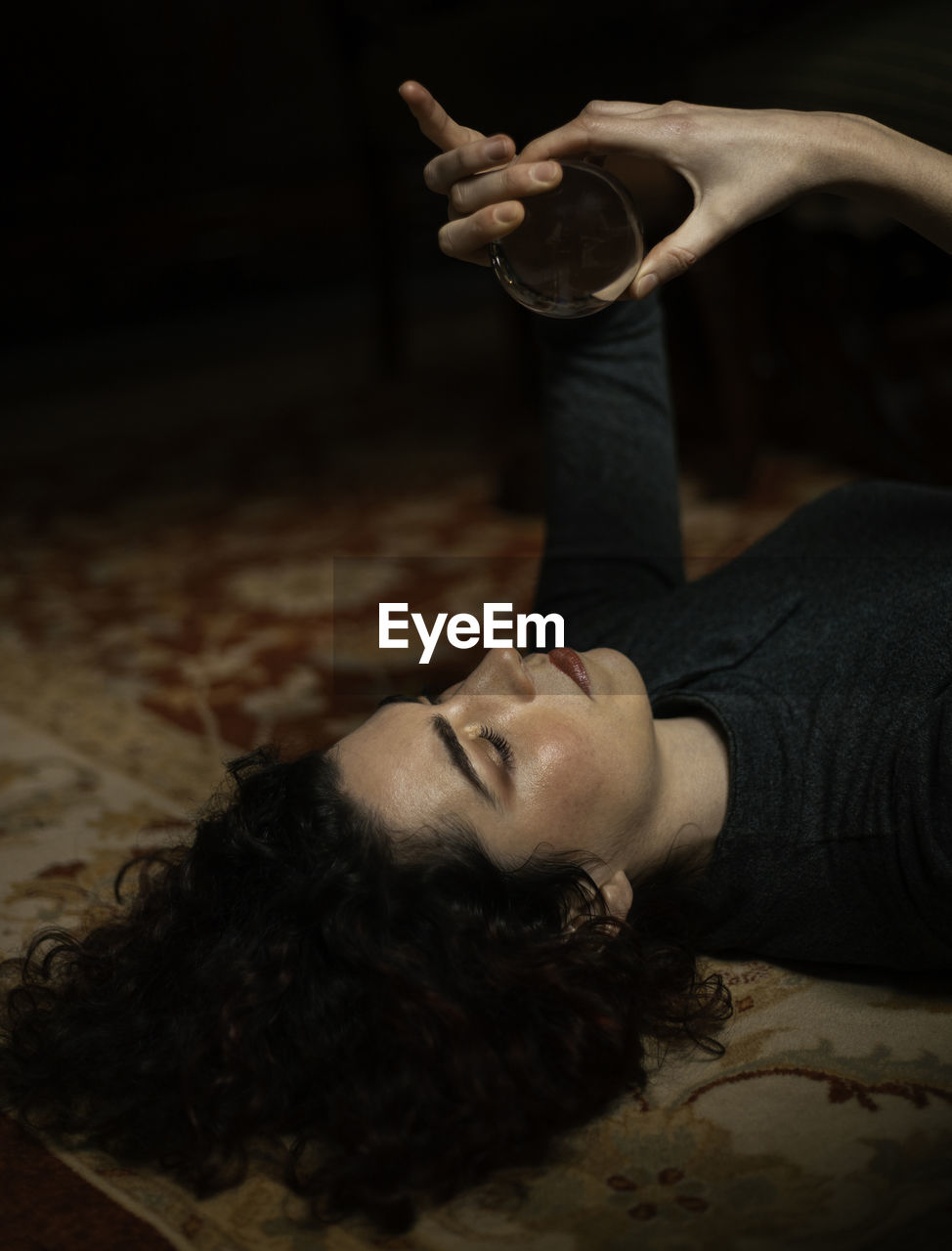 Side view of relaxed female with black hair lying on carpet with transparent crystal ball in room with retro design