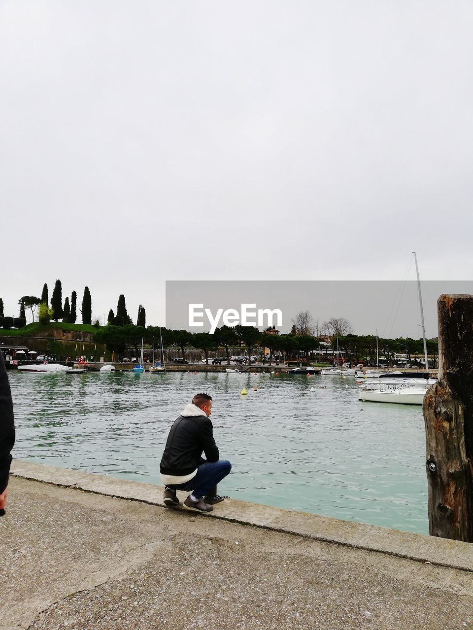 MAN SITTING ON LAKE AGAINST SKY